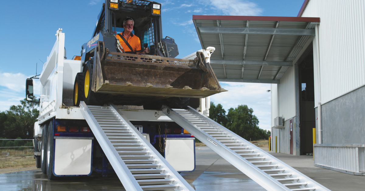 Image of a skid steer unloading from the rear of a truck using a pair of loading ramps