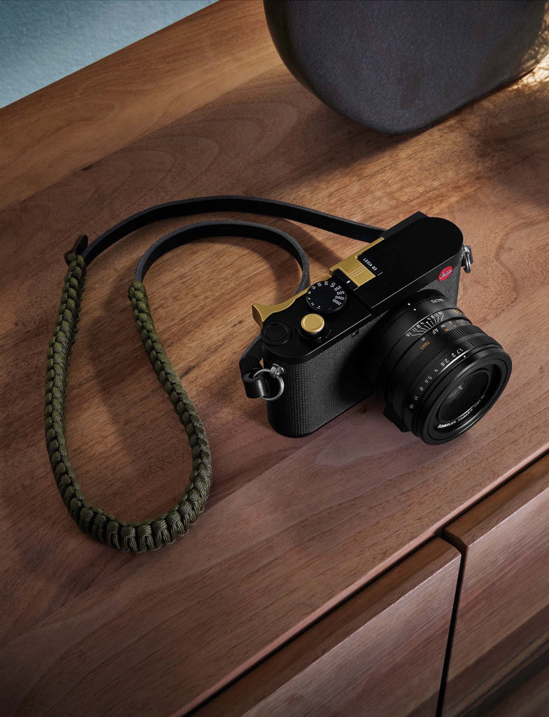 Overhead photo of Leica Q3 camera with green rope strap on a brown wood table top