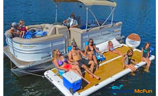 A family of 6 sit on an inflatable dock that is connected to a pontoon boat. They sit in chairs on the dock along with a cooler. A small child rests her head on a pillow.