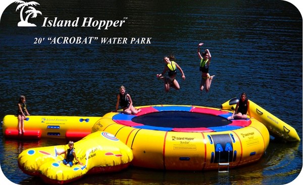 Island Hopper Acrobat 20ft Water Trampoline Park. 2 girls jump up in the air while 4 others sit and play on the pad and the water attachments.