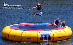 Island Hopper 20ft Acrobat Water Trampoline - 1 man jump, while 2 friends sit on the edge of the yellow, round Acrobat Water Trampoline