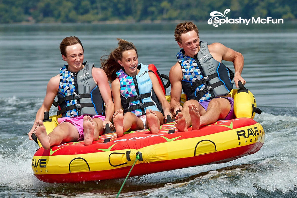 This is the red and yellow RAVE #Epic 3-Person Towable Boat Tube on the water with 3 people on it while being dragged by the boat.