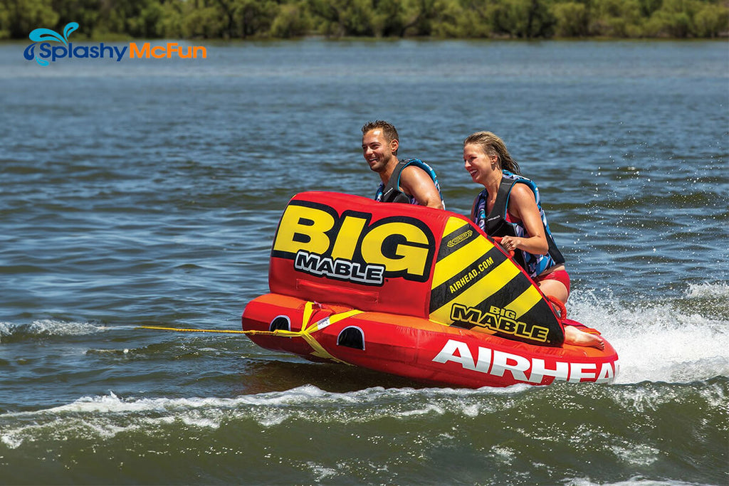 This is a Dual Tow Point Tube with 2 people kneeling on it, holding onto the handles while being dragged by a speedboat on the water.