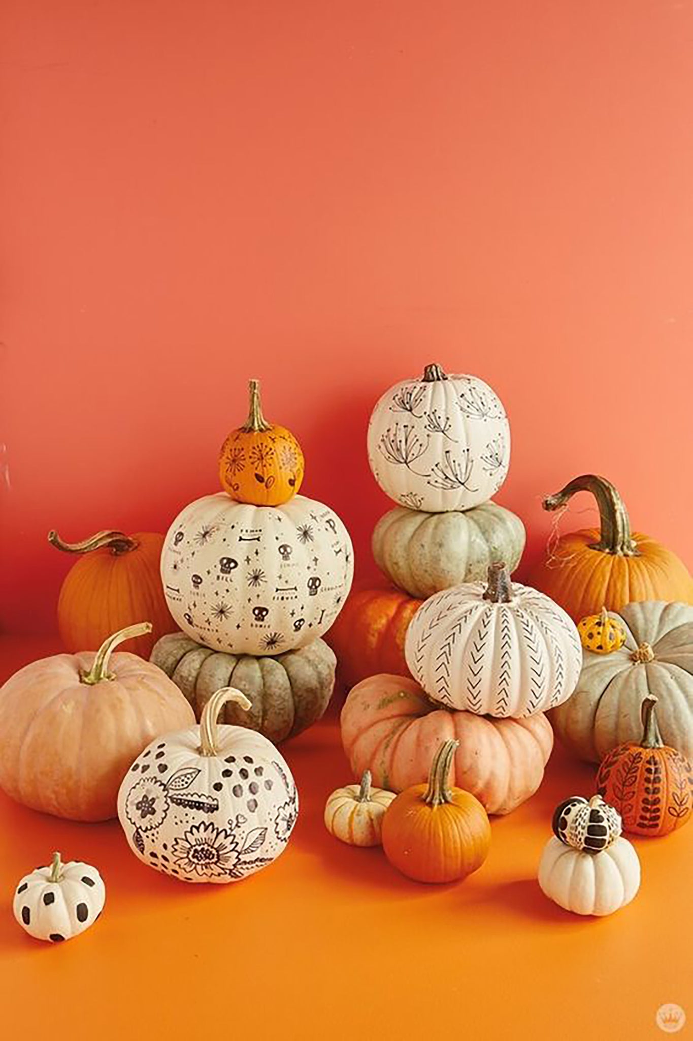 An arrangement of different sized painted pumpkins in front of an orange wall