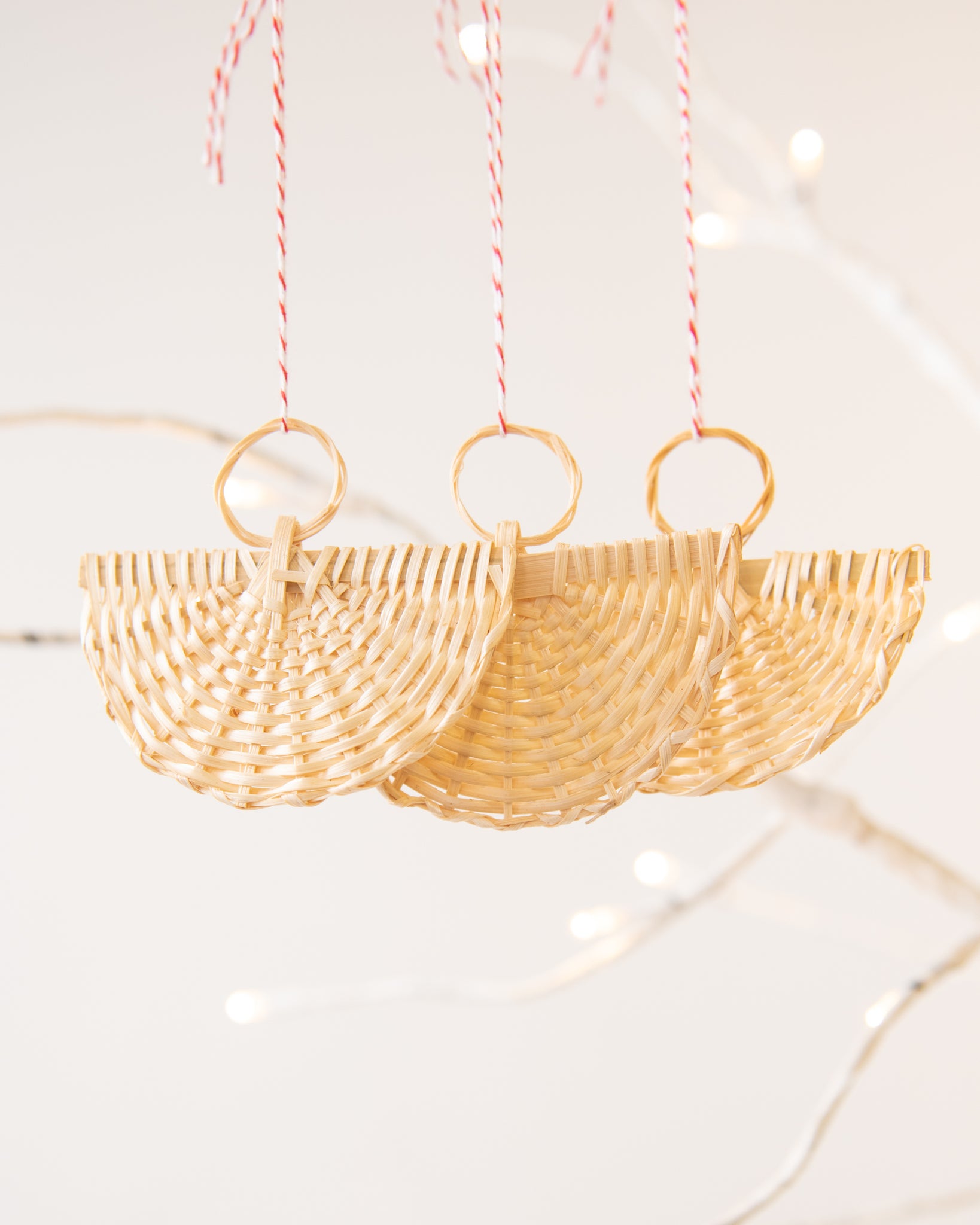 rattan angel ornaments with red and white striped string on a birch tree with tree lights, white background
