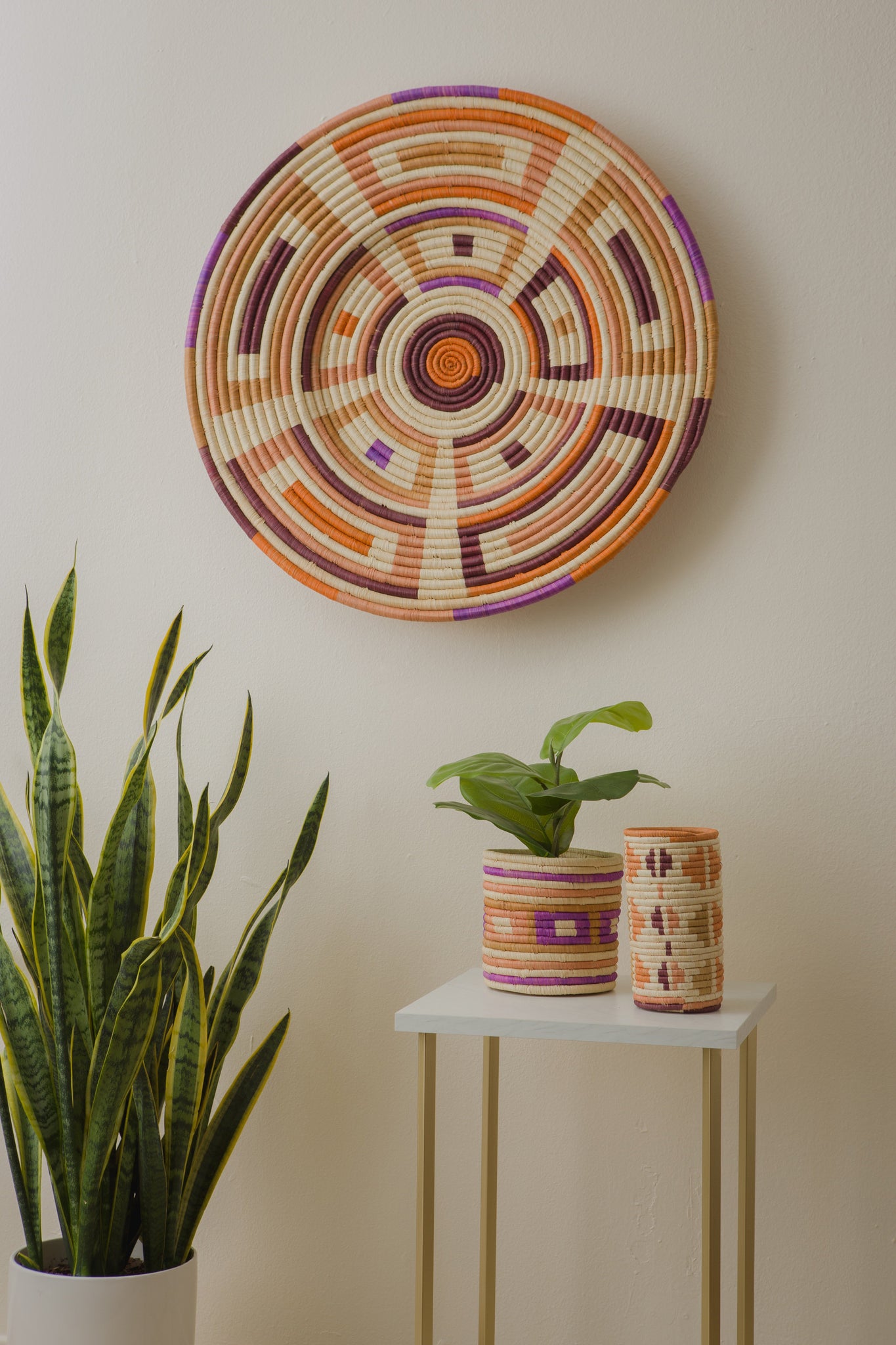 vignette of geometric purple and orange woven wall plate. Geometric planter with plant and vase on a side table