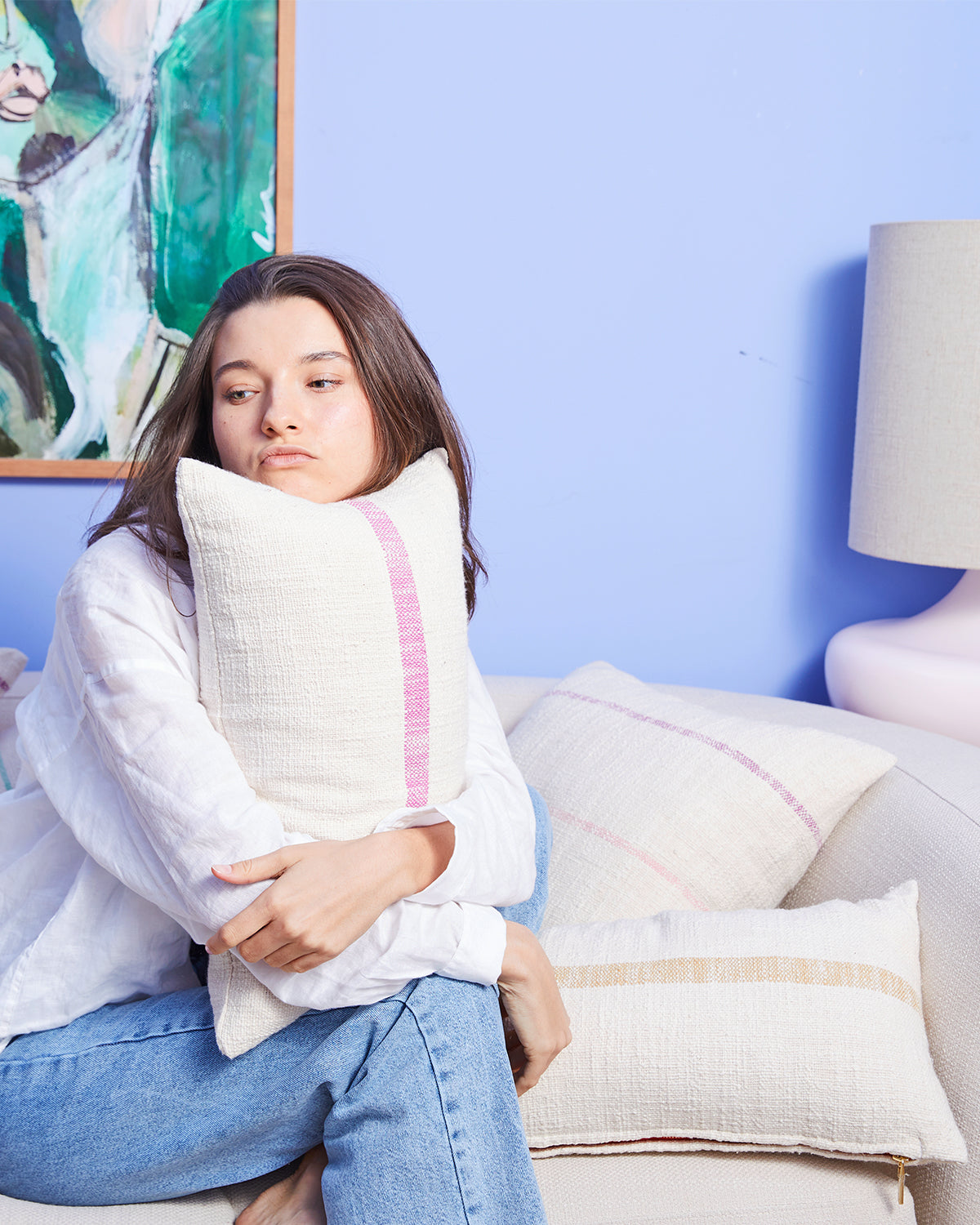 Woman sitting holding a striped pillow on a couch filled with pillows