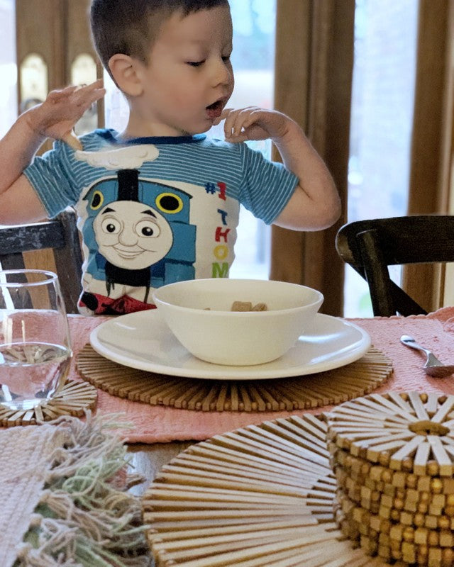 little boy sitting at table, table covered with coasters and placemats