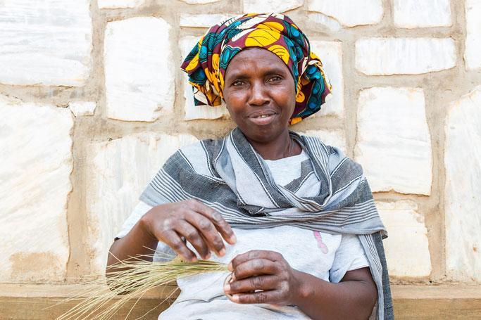 African woman weaving basket in front of wall