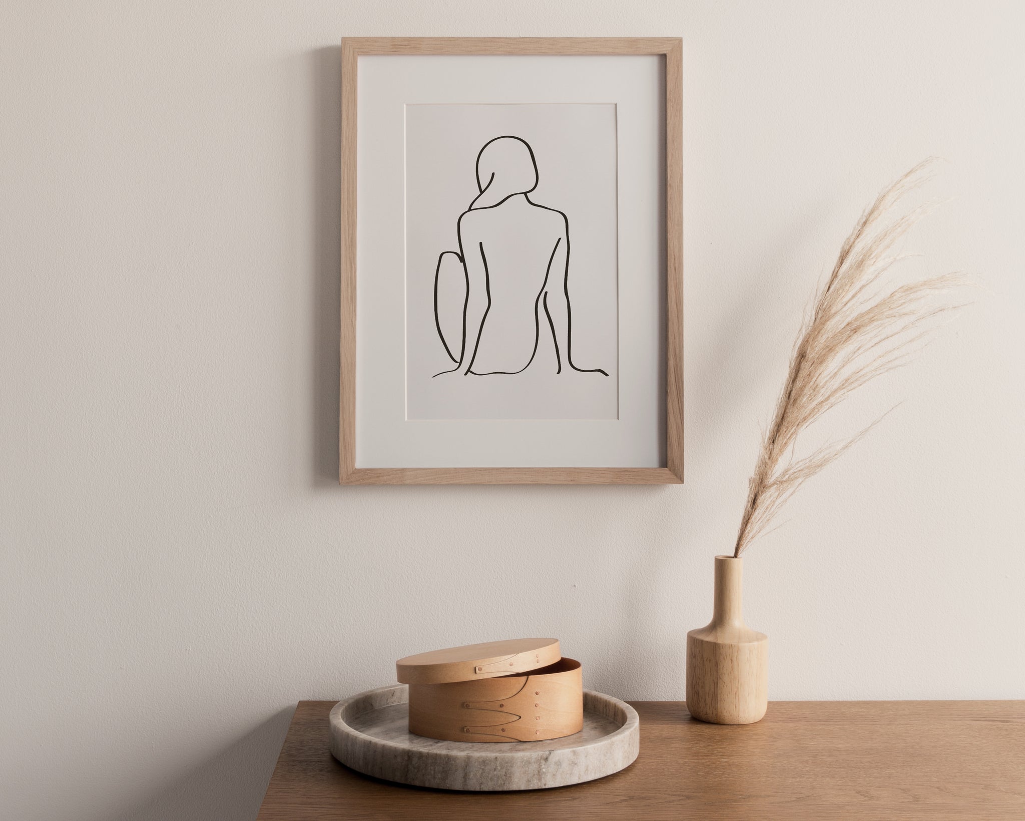 framed print of a drawing of a girl sitting. frame on a cream wall with table below