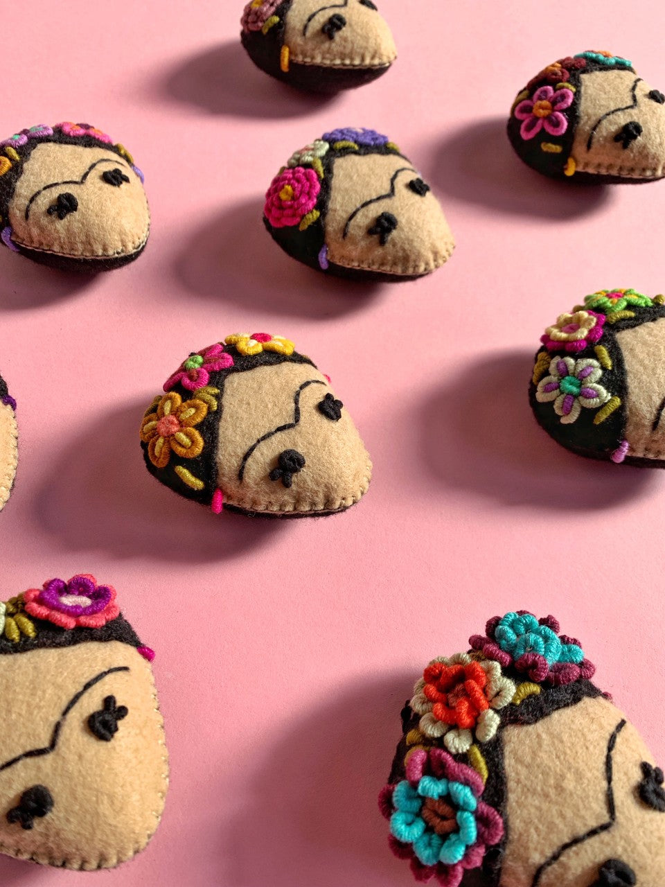 hand sewn Frida Kahlo head ornaments laid out on a pink table