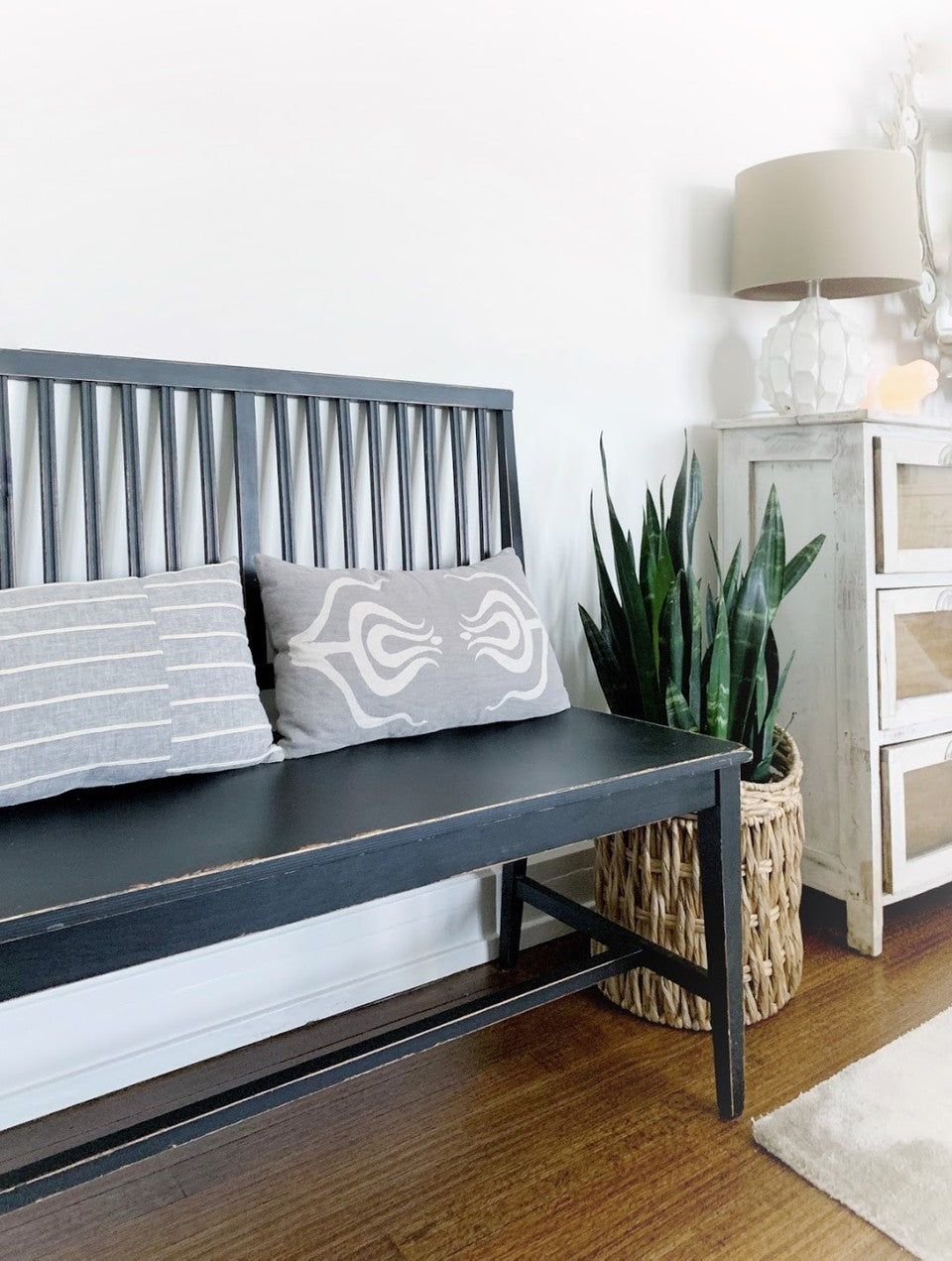 black wooden bench in front of white wall with two grey lumbar pillows on top