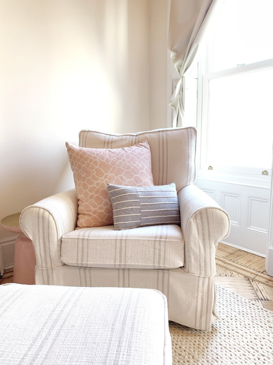 white and grey striped arm chair with large pink pillow and grey lumbar pillow on top in front of white wall