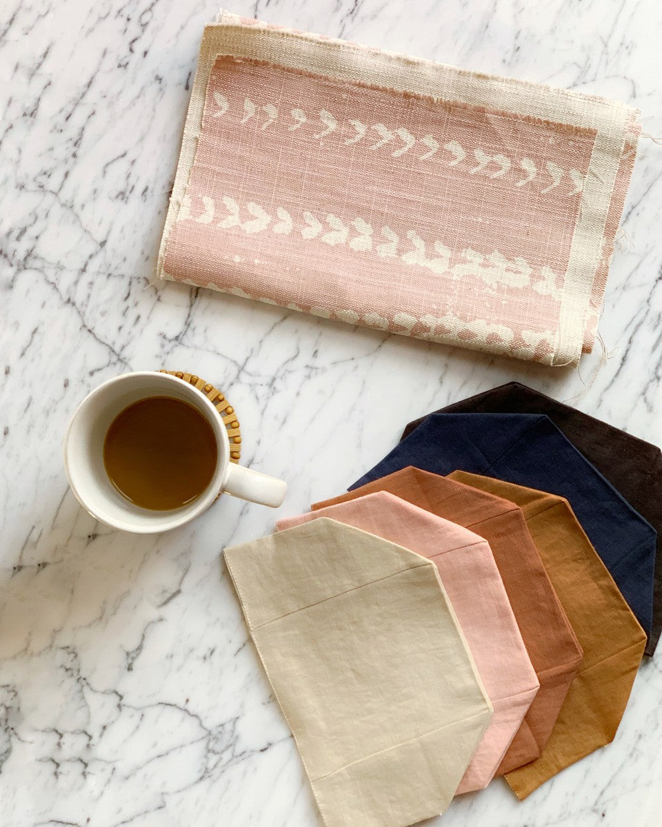 marble table with cup of coffee, six linen tissue box colors splayed in various earthy colors, folded pink fabric