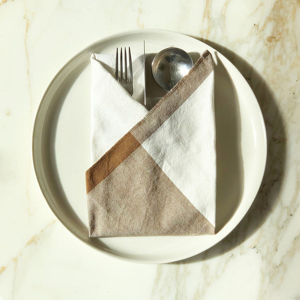 Image of M+A NYC Colorblock Napkin in the colorway Kora/Earth folded on a plate with flatware tucked inside.