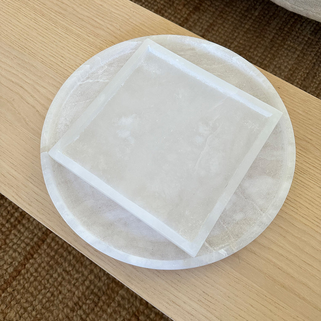 M+A NYC Alabaster Trays, Round and Square, on a low wooden table.