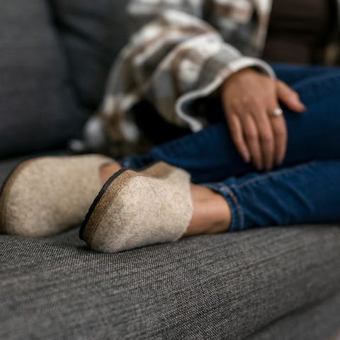 A person sitting on the couch with their feet up on the couch showing off their Women's Ecowool Clog - Coburger Fox Sheep colorway.