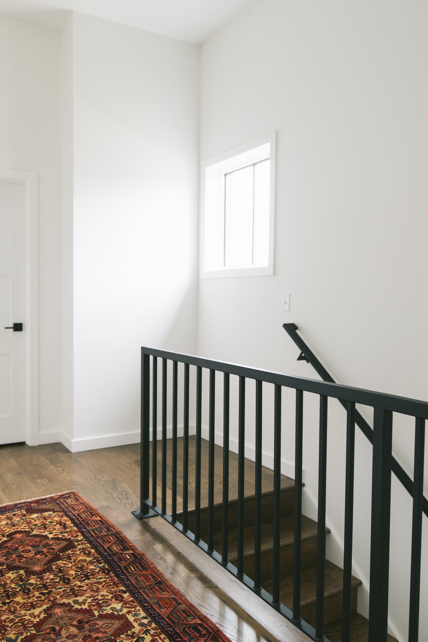 A long floor runner rug in a hardwood floor hallway. The vintage rug has intricate geometric patterns in red, orange, yellow, brown, and black.