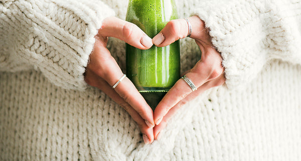 Woman in cozy sweater holds green immunity boosting smoothie in heart hands while sick.