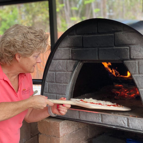 Pam putting pizza in Maximus Prime wood-fired oven