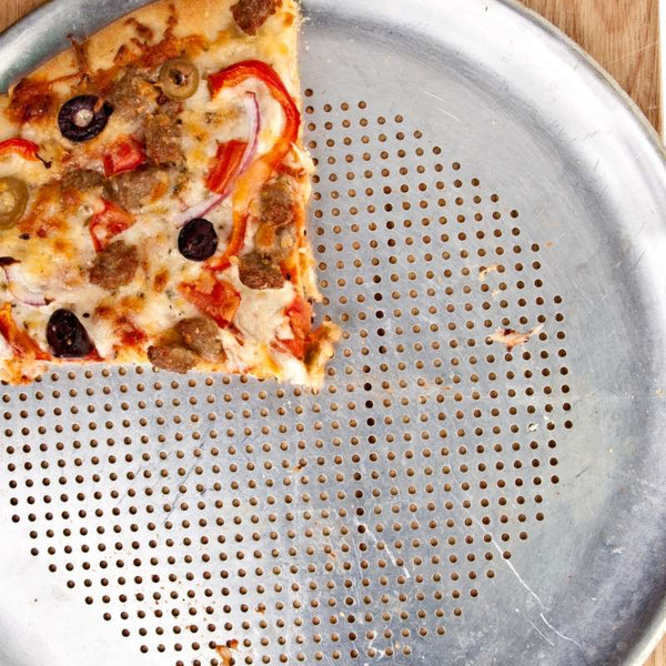 Silver pizza pan with holes and one slice of pizza on it