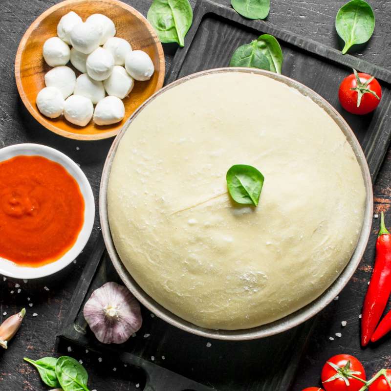 Homemade pizza dough in bowl with mozzarella balls beside it