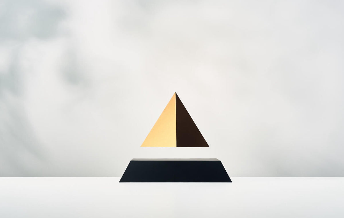 Levitating pyramid Py with black base and gold top on a light background