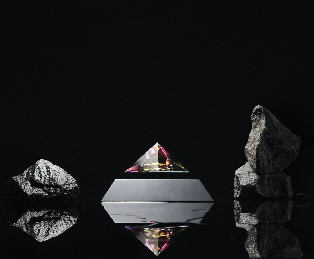 Levitating pyramid Py by Flyte, iridescent crystal top and black base version surrounded by rocks
