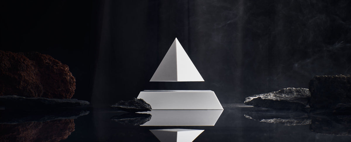 Levitating pyramid Py by Flyte, white top with white base option surrounded by rocks in a dark setting