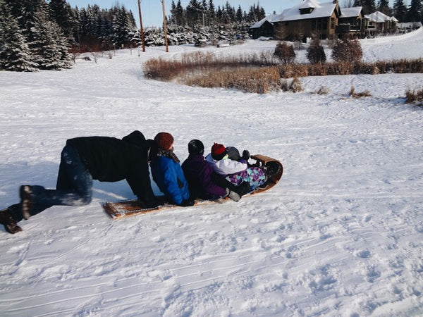 Man running, pushing his friends down a hill in their toboggan