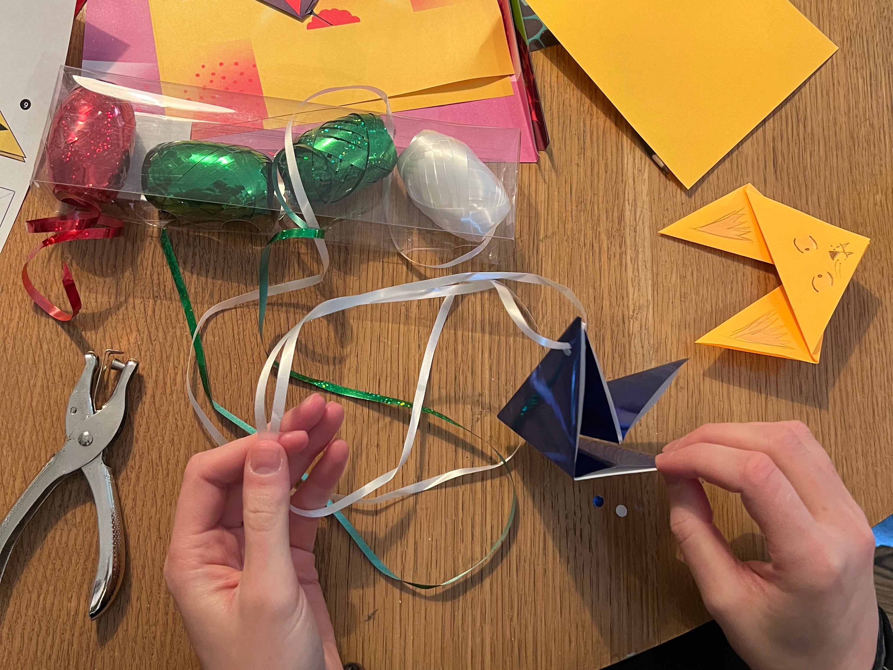 hands putting gift wrap string through a hole punched origami shape to make an ornament