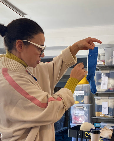 Tia standing in her design studio holding up a blue sock, she is sticking pins in it to show where wave will go for new style