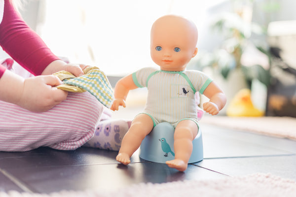 Pomea doll sitting on a potty with toddler holding towel