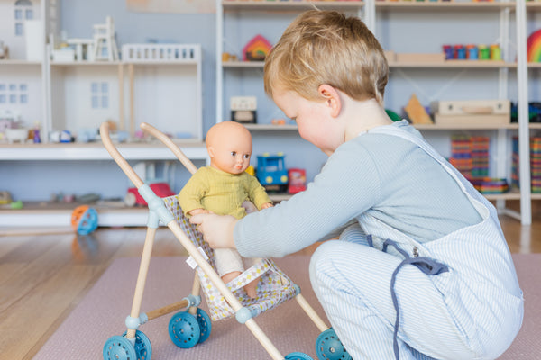 Toddler putting djeco pomea doll into stroller in playroom