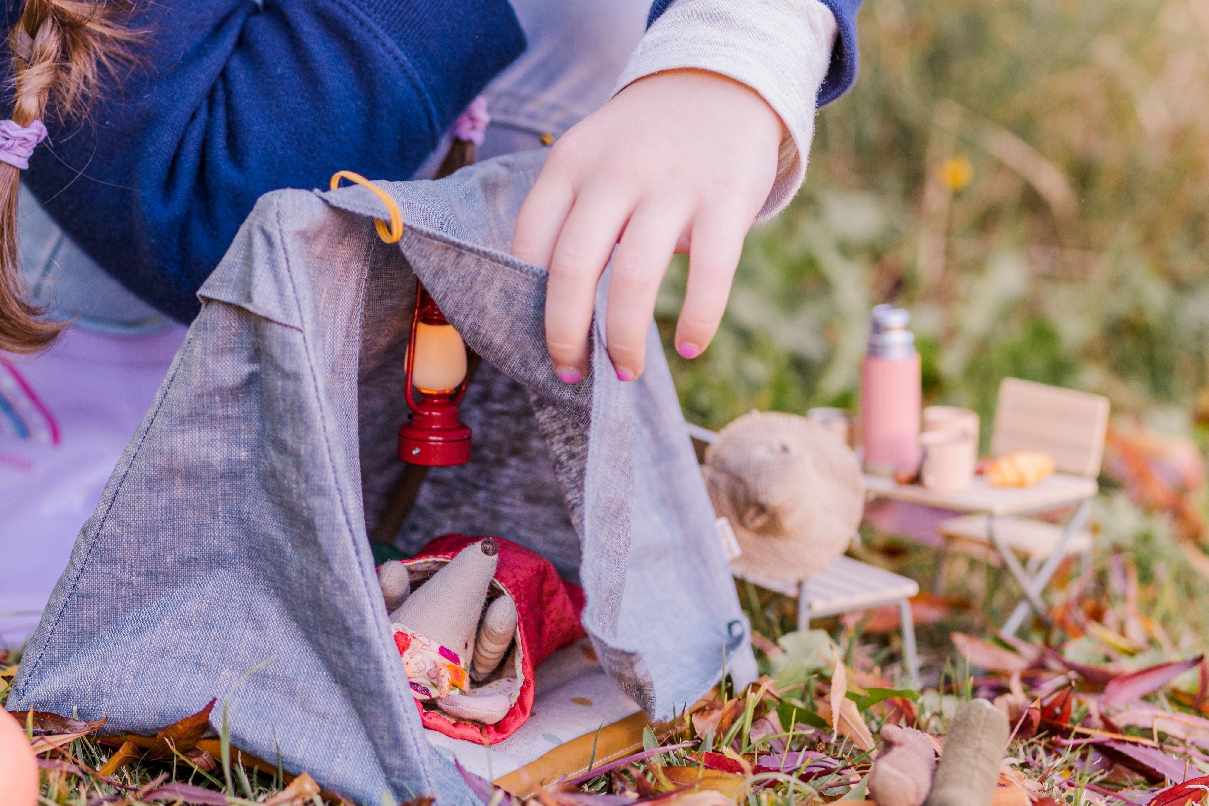 Child playing with <img src="https://cdn.shopify.com/s/files/1/1278/1015/files/Autumn_camping_shoot_-_Maileg_2023_5.jpg?v=1684220370" alt="Maileg hiker mouse big brother and big sister sitting near tent and campfire