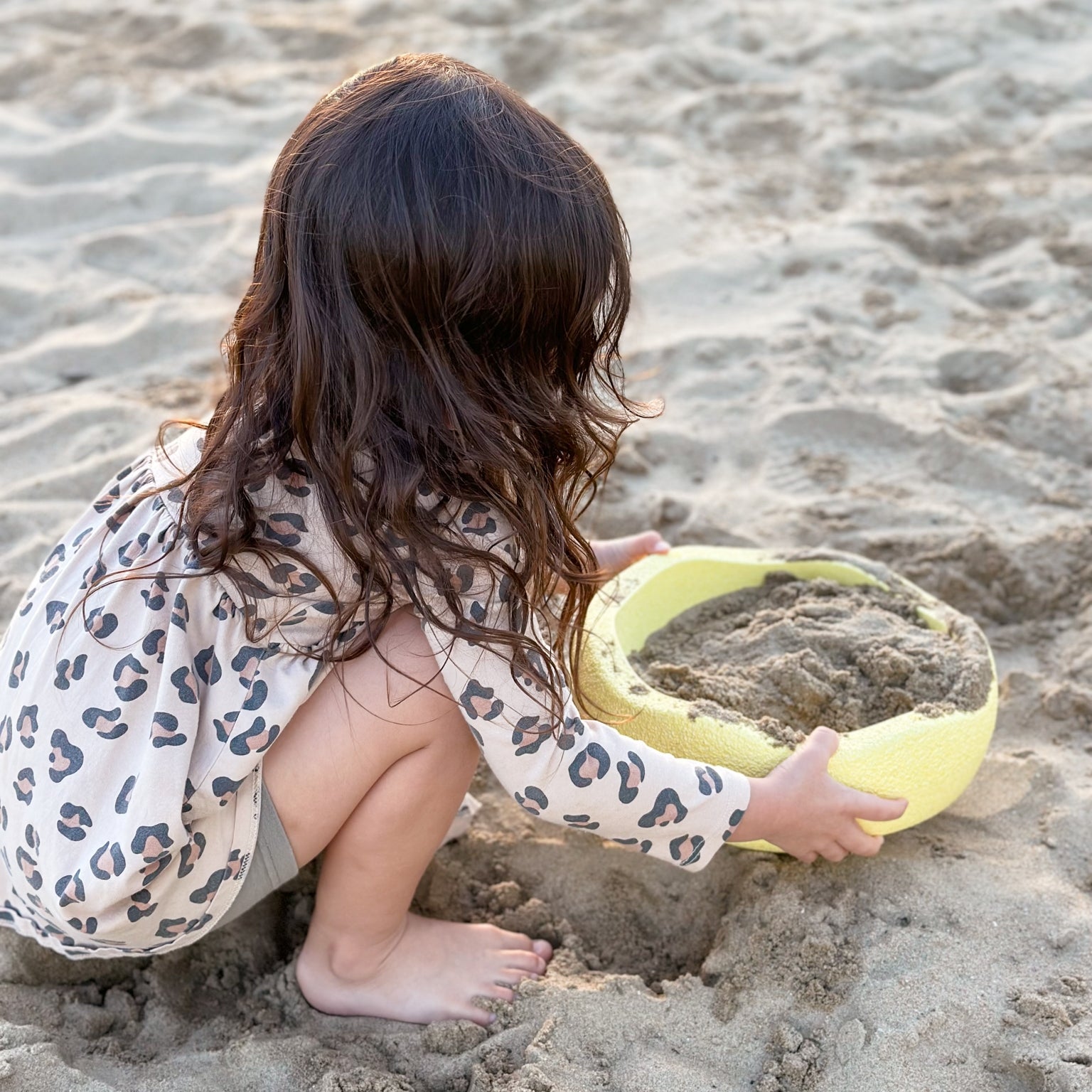 Child holding yellow pastel stacking stone filled with sand from Stapelstein in playground