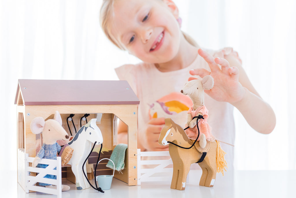 Child smiling playing with Maileg mice and wooden barn and horses 