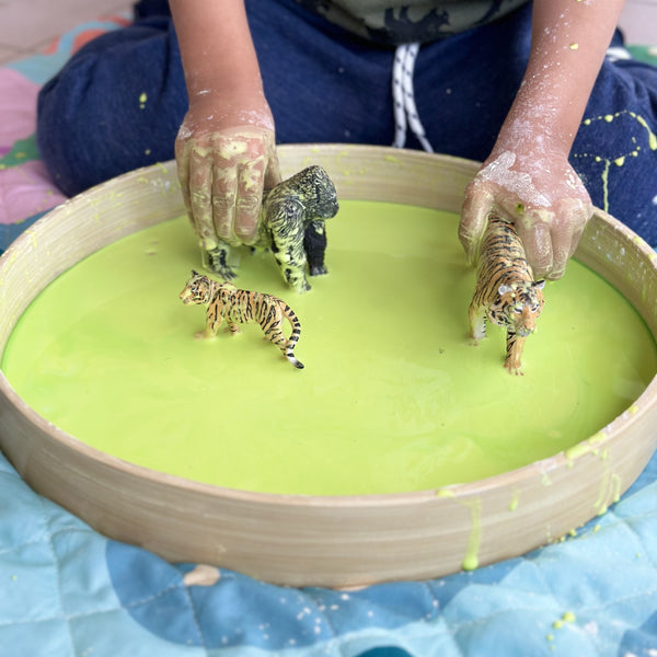 Child playing with green oobleck in sensory tray