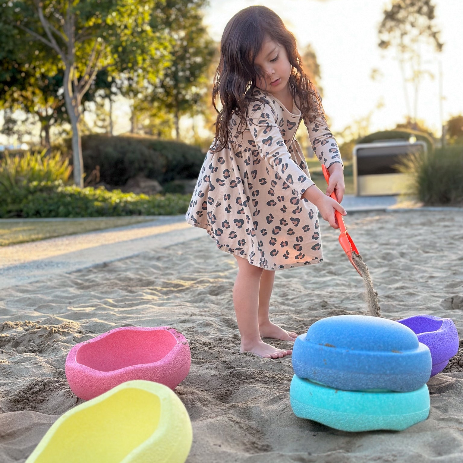 Child pouring sand into pastel stacking stones from Stapelstein in playground