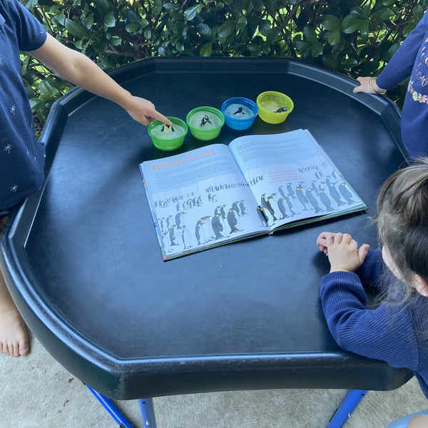 Tuff tray with frozen penguins and book and 3 children around the tray