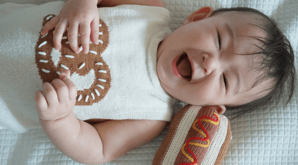 Certified Organic Cotton Baby Toy & Clothe - Picture of newborn with hot dog rattle & wearing knit romper.