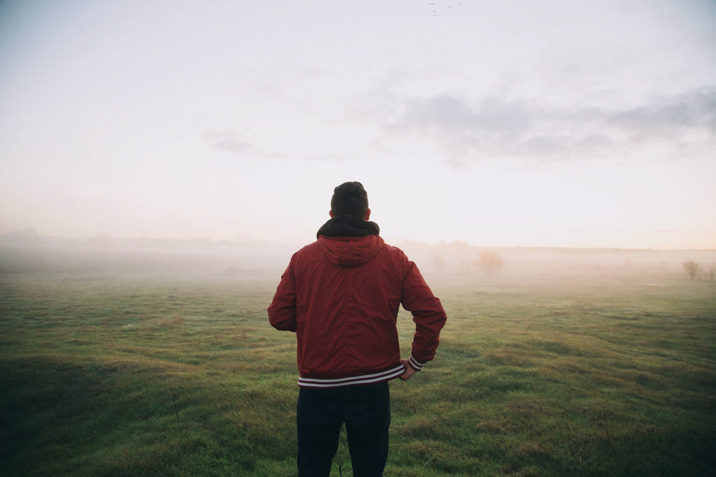 A runner is looking at an open field with misty weather.