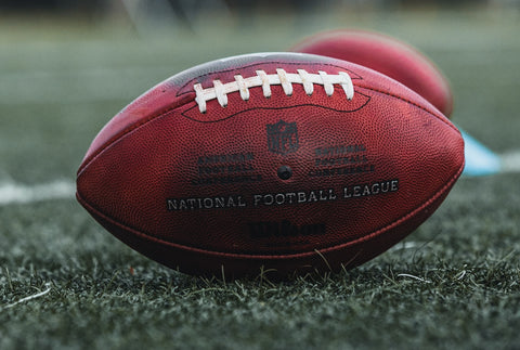 A National Football League (NFL) football rests on a field near yard lines.