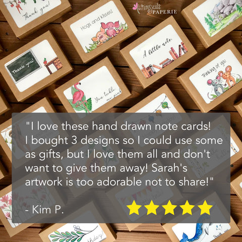 boxes of illustrated note cards lying on a wooden surface with a review stating: "I love these hand drawn note cards!  I bought 3 designs so I could use some as gifts, but I love them all and don't want to give them away! Sarah's artwork is too adorable not to share!"