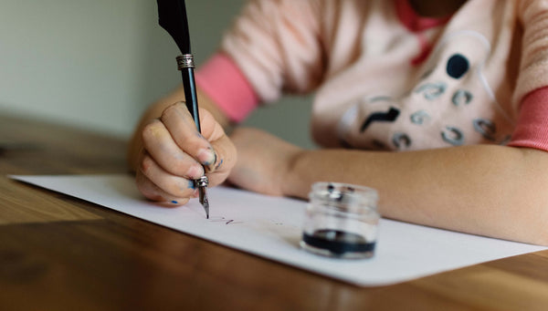 small child writing with a fountain pen with ink blotches on their fingers