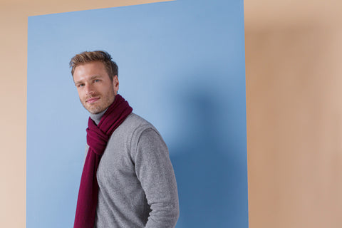 Man wearing a grey jumper and a long, red scarf, both made of pure cashmere, looking towards you