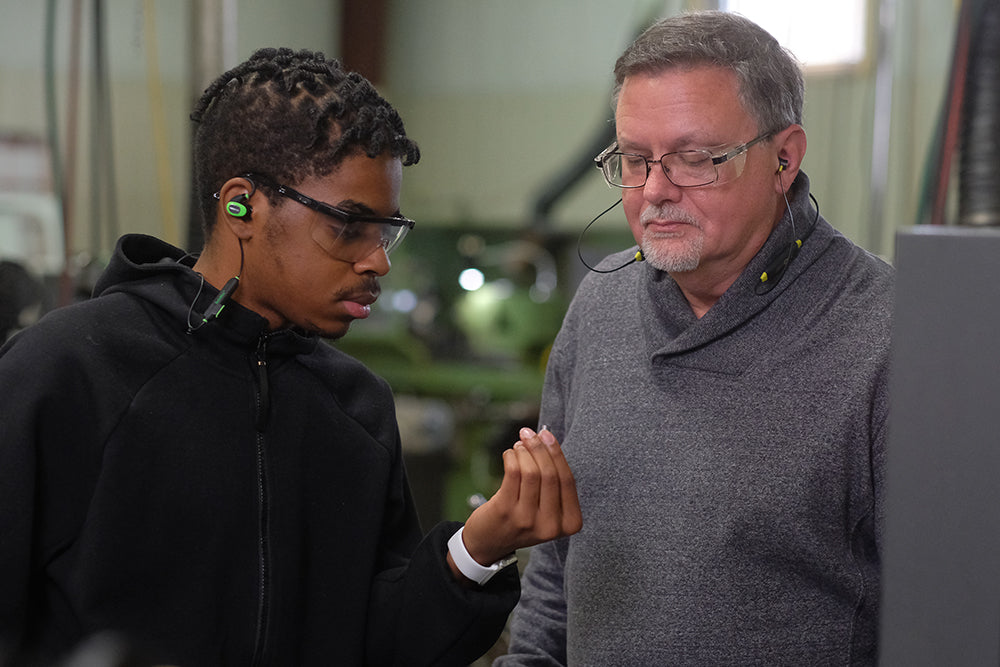 Two men talk and discuss a project while wearing their ISOtunes hearing protectors.