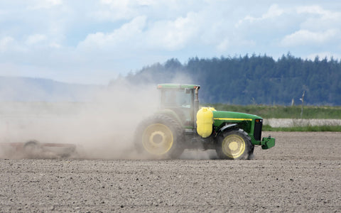 A farm tractor plowing the field with dust following behind it