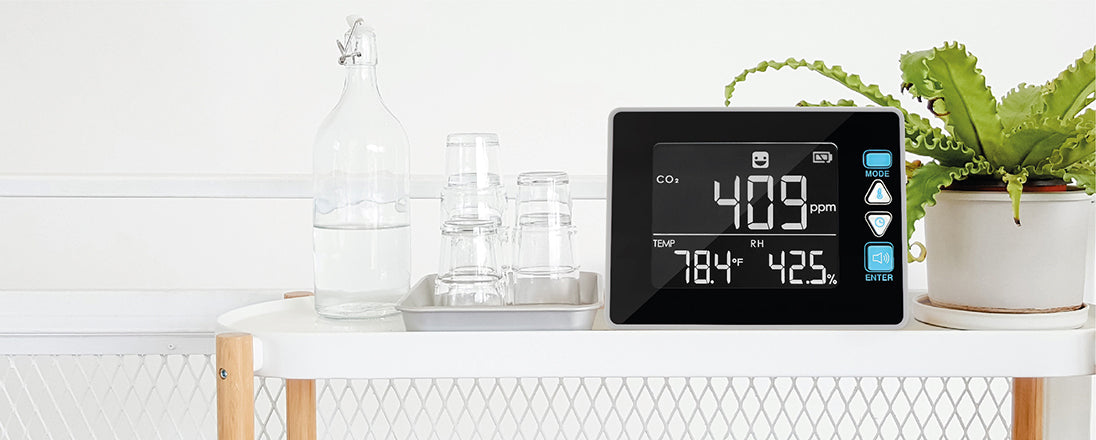 CO2 Meter on a white shelf with green plant aside