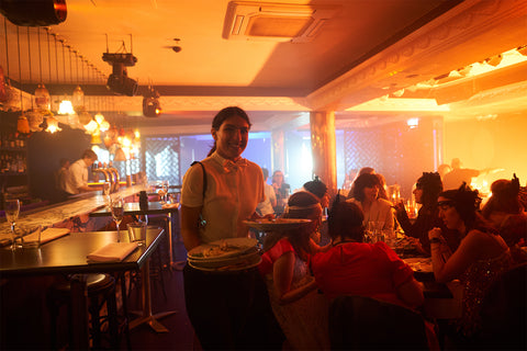 Sydney's coolest bottomless brunch idea, a burlesque show in the Bamboozle Room in Potts Point. Server is standing in front of a full crowd, with light coming through the windows as the crowd wine and dine on bottomless bubbles and 3 course meal watching Sydney's best burlesque showgirls.